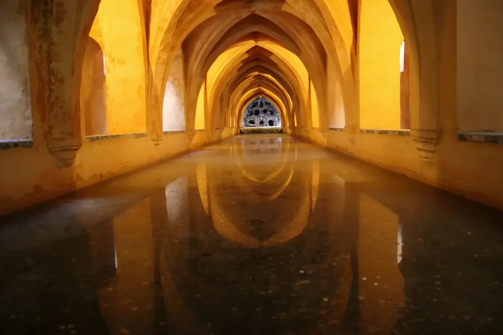Das gewölbte unterirdische Becken, bekannt als Bäder der María de Padilla, gotische Rippen spiegeln sich im stillen Wasser