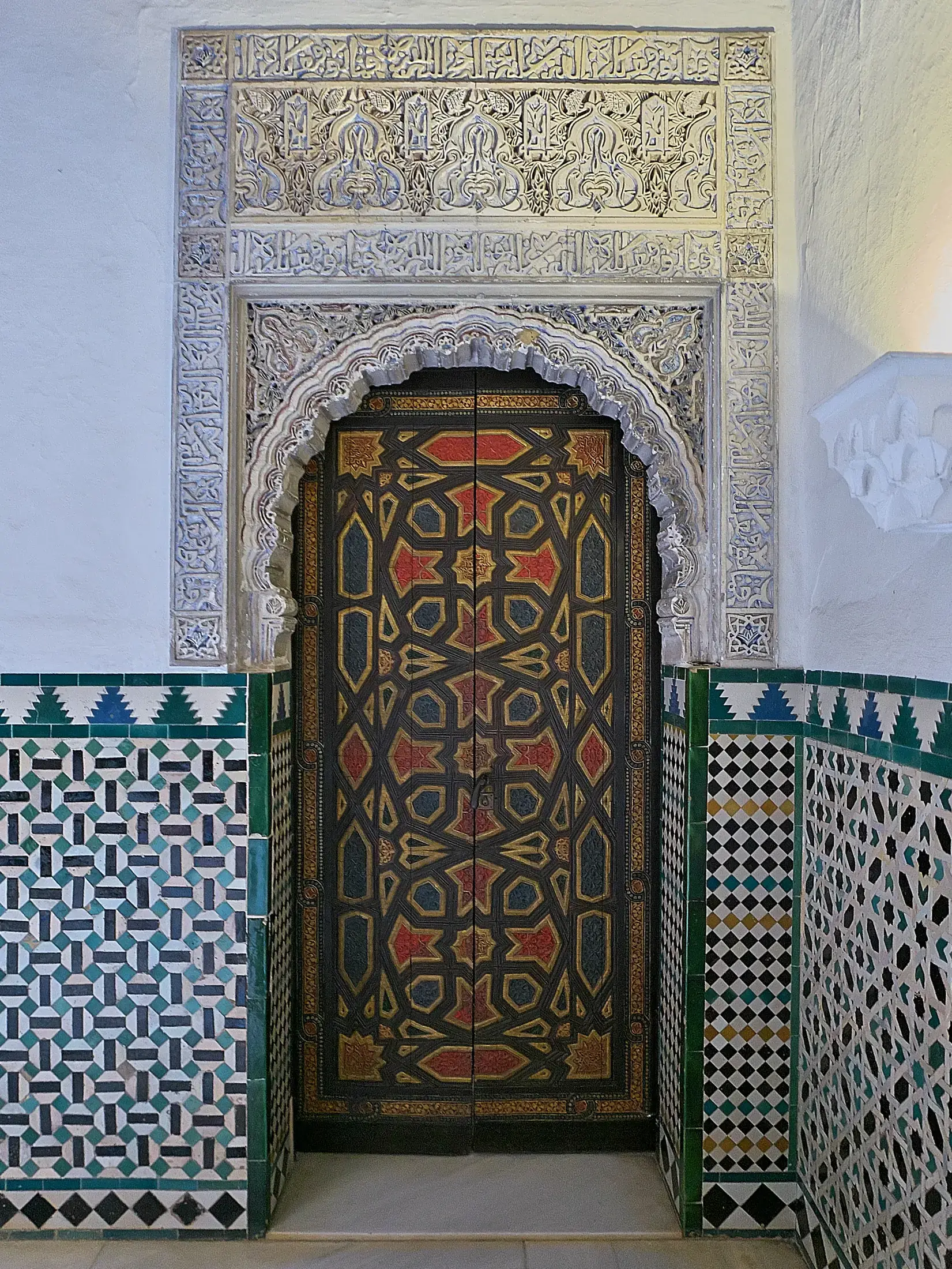 Bemalte und vergoldete Tür des Patio de las Doncellas, oben von geschnitztem Stuck und unten von Fliesenmosaik gerahmt