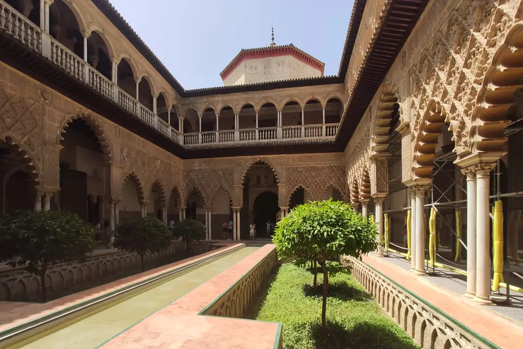 The Patio de las Doncellas: a long sunken pool between orange trees, framed by carved Mudéjar arches